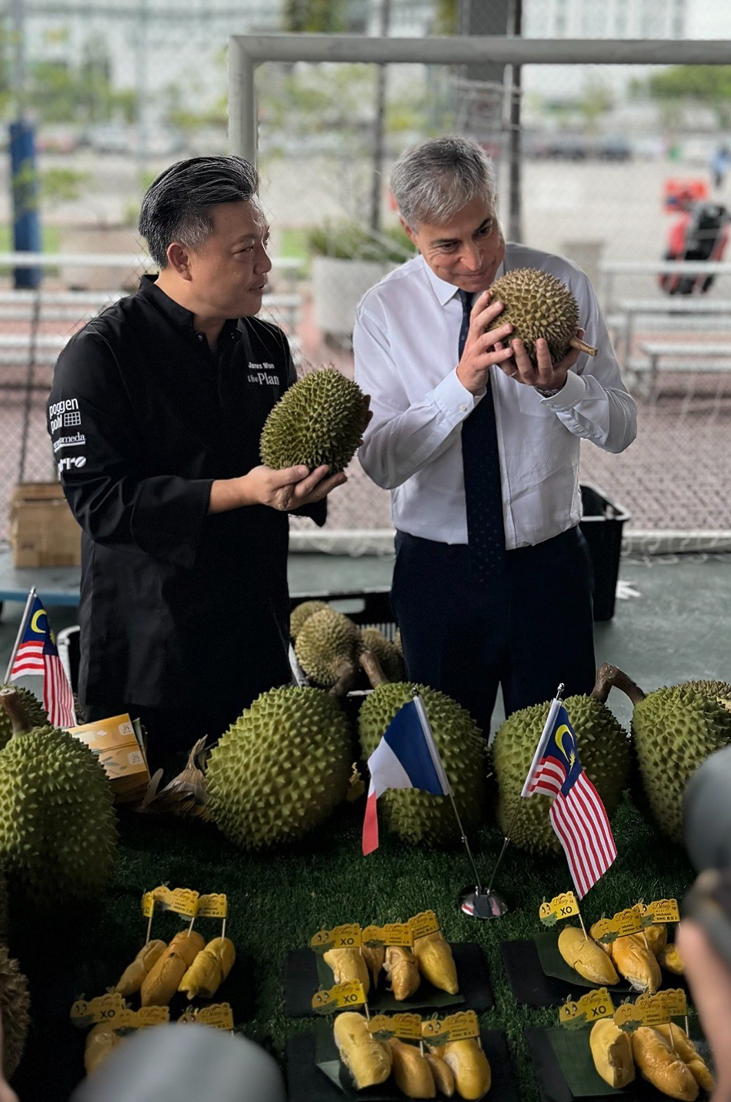 Chef James Won and Ambassador Marc Abensour examining durians, French and Malaysian flags between them